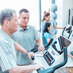 Dyaco Medical Physical Therapy Upright Bike 4.0U in gym room showing a close up of patient gripping pulse grip heart sensors and therapist standing by his side.