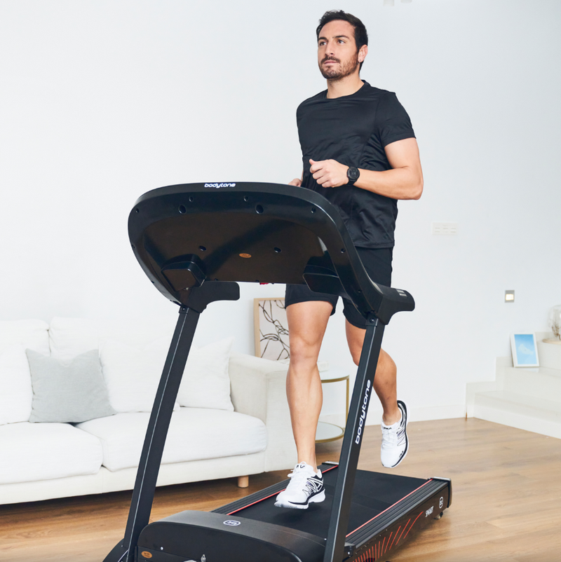 Man using a Bodytone Active Run LED treadmill viewed from the front in a living room setting.