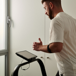 Man using Bodytone ZROTH Curved Treadmill with a tablet attached, standing by a window.