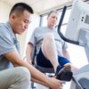 Dyaco Medical Physical Therapy Recumbent Bike 4.0R in gym room with therapist helping patient place his foot into the pedal.
