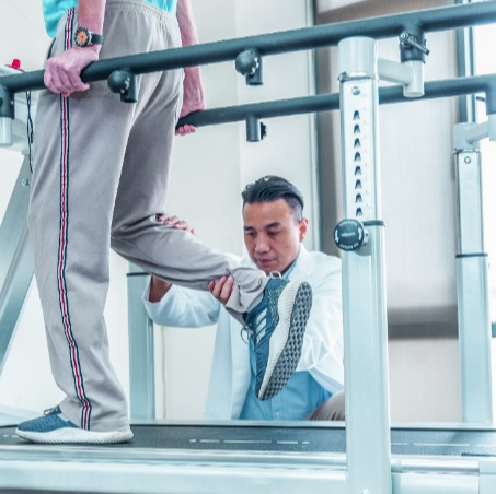 Dyaco Medical Rehabilitation Treadmill 7.0T with therapist holding the lower leg of the patient, guiding him to place his foot down correctly.