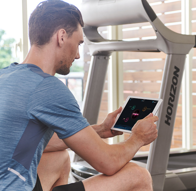 Horizon Paragon X @Zone Treadmill in room with male model sitting in front of it viewing data on tablet