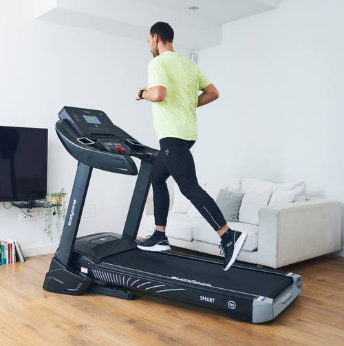 Man running on a Bodytone Active Run 600 Smart treadmill in a living room setting