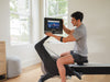Nordic Track RW700 Rower. An image showing a male sitting on the rower whilst altering the angle of the console.