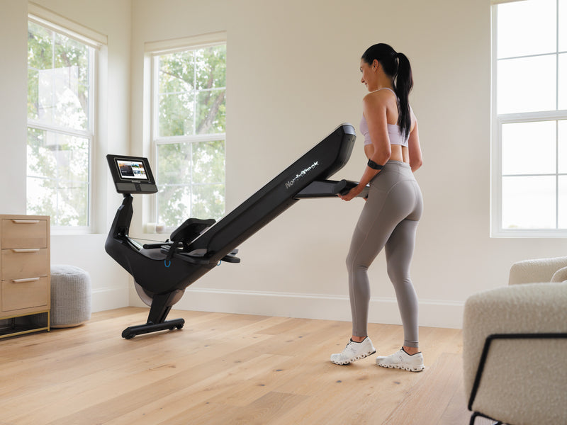 Nordic Track RW700 Rower. Image of a woman moving the rower using the transport wheels at the front of the machine.
