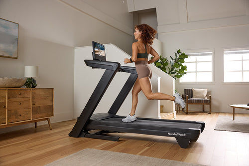 A person running on a NordicTrack Commercial 1750 Treadmill in a home environment.