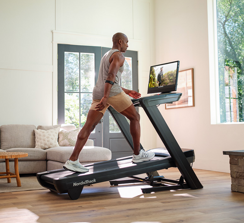 A person exercising on a NordicTrack Commercial 2450 Treadmill with a male focusing on the treadmill's 24-inch HD touchscreen.