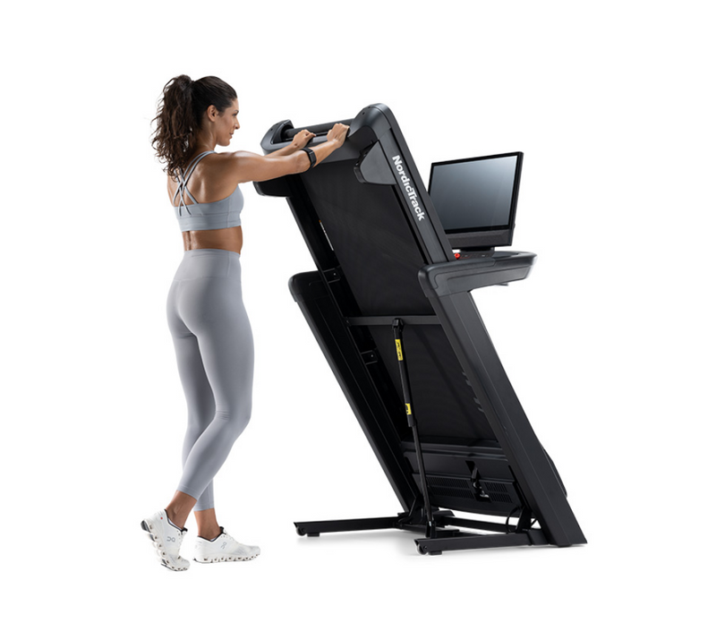 NordicTrack Commercial 2450 Treadmill with woman folding it against white background
