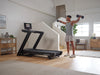 NordicTrack Commercial LE Treadmill with man in room setting lifting dumbbells.
