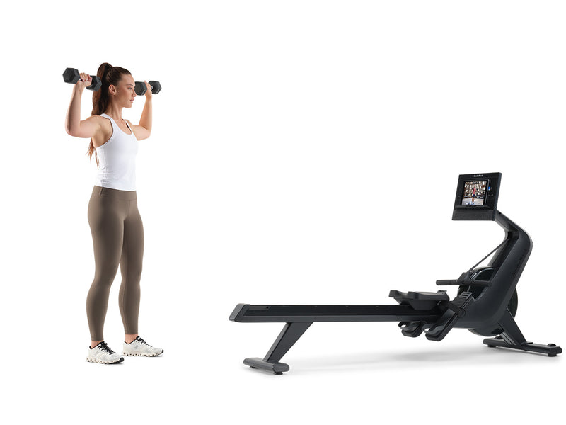 Woman standing next to NordicTrack RW300 Rowing machine using dumbbells against a white ackground