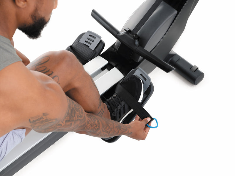 Nordic Track RW700 Rower. Image of male sitting on the rower demonstrating how to use the foot straps on the footplates.