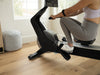 Nordic Track RW700 Rower. Image showing a woman at front of the  machine at the beginning of the stroke in room setting