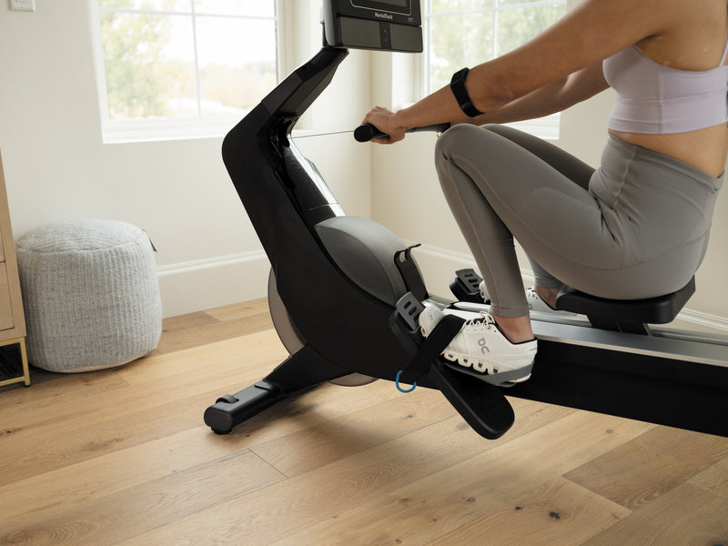 Nordic Track RW700 Rower. Image showing a woman at front of the  machine at the beginning of the stroke in room setting