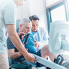 Dyaco Medical Rehabilitation Recumbent Seated Stepper 7.0S with two therapists helping patient get the correct seat and hand positions while seated on stepper.