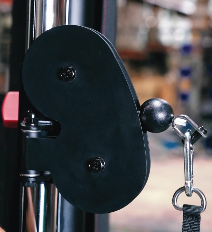 Close-up of a black pulley system on a gym machine with a blurred background.