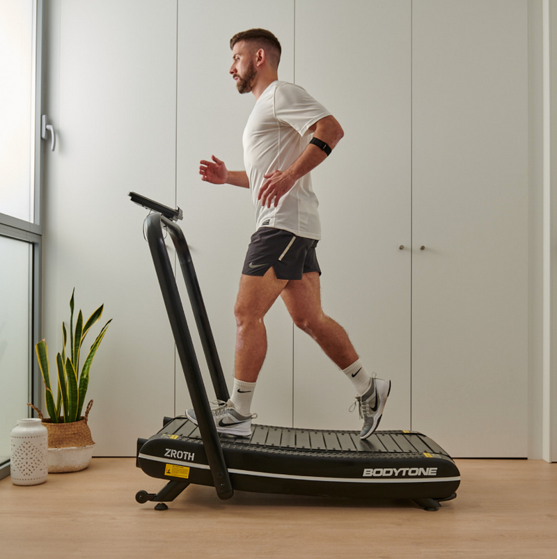 Man exercising on a ZROTH BODYTONE treadmill in a room with a plant and window.