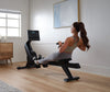 A person using the NordicTrack RW 300 Rower machine, which is a modern rowing machine with a digital display and black color palette, in a home exercise environment.